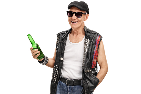 Senior punk rocker with a leather vest with pins holding a bottle of beer isolated on white background